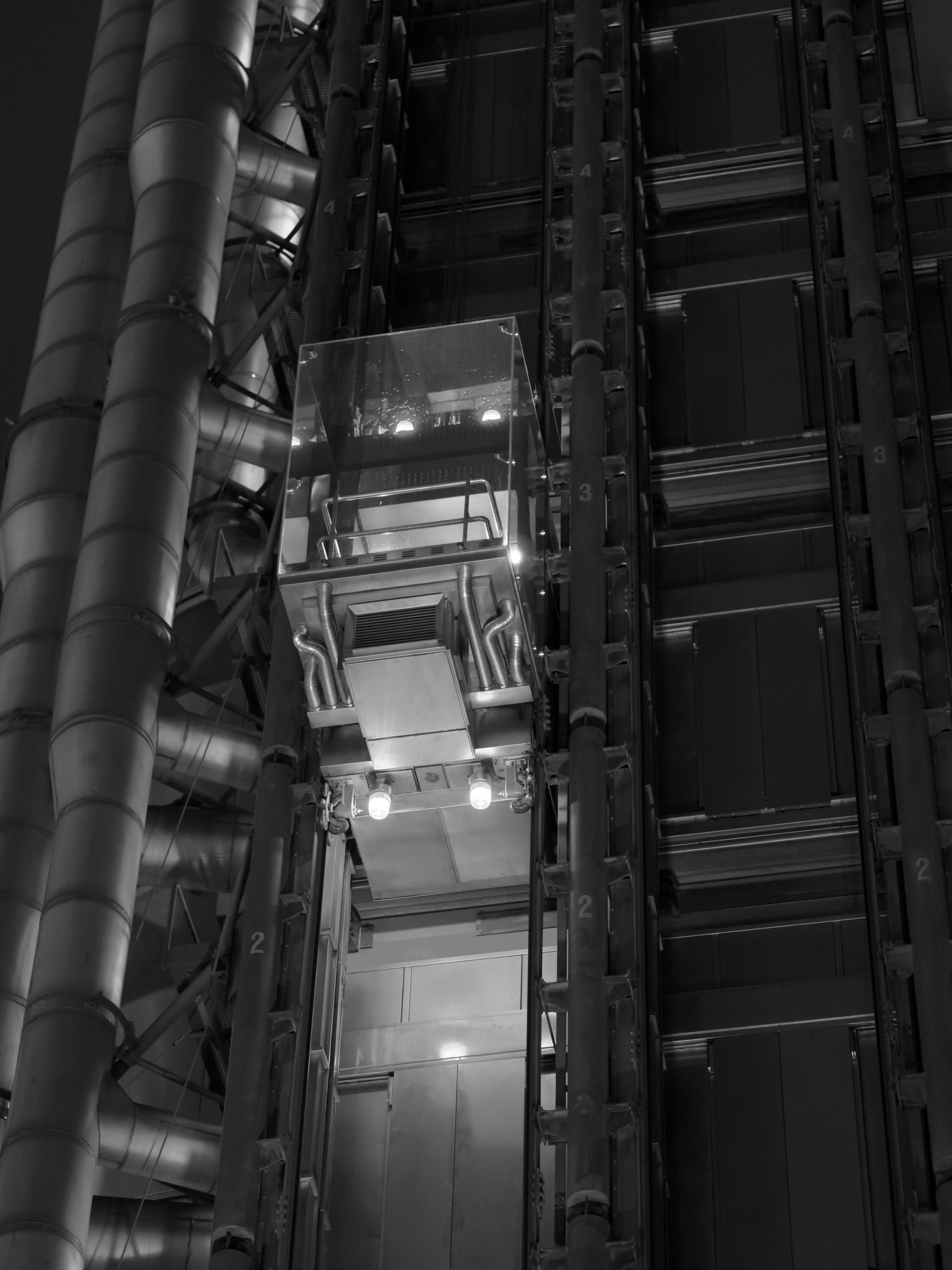 A glass lift car riding the outside of the Lloyd's building at night, lit in red and blue